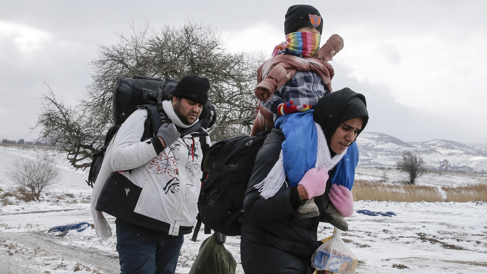 Un couple, dont la mère porte son enfant sur son dos, traverse un champ couvert de neige en Serbie Un couple, dont la mère porte son enfant sur son dos, traverse un champ couvert de neige en Serbie