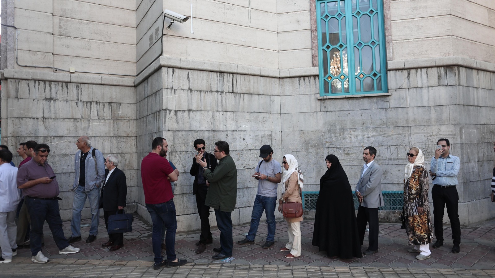 Des hommes et des femmes voilées attendent en file devant un vieil immeuble. Des hommes et des femmes voilées attendent en file devant un vieil immeuble.