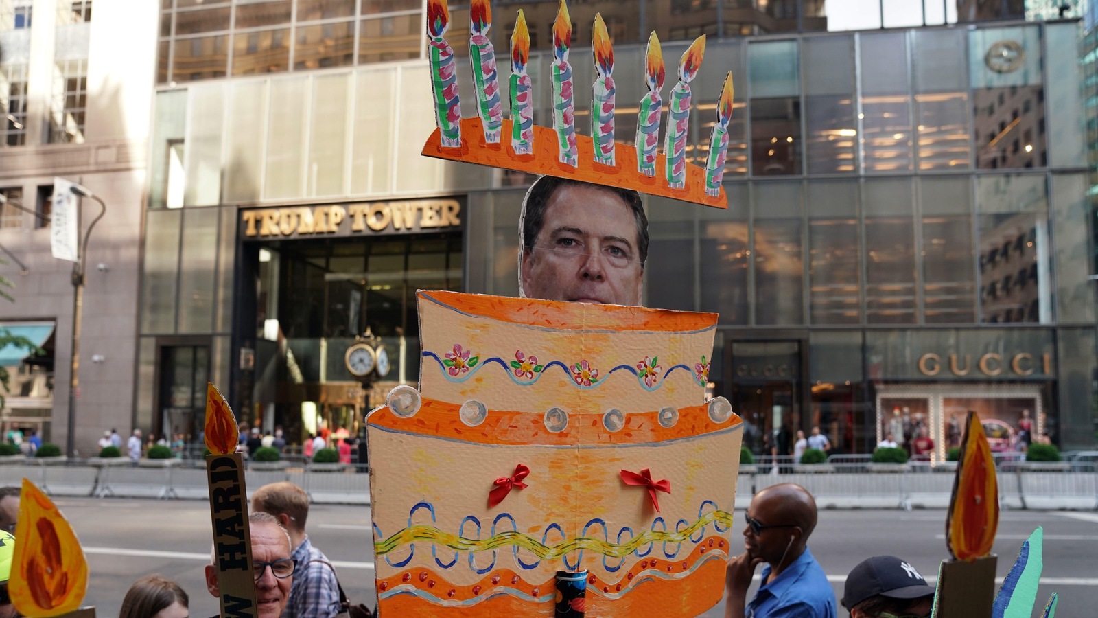 Des manifestants anti-Trump brandissent une pancarte en forme de gâteau de fête pour l'anniversaire du président des États-Unis. L'ex-directeur du FBI James Comey est caché à l'intérieur du gâteau. Des manifestants anti-Trump brandissent une pancarte en forme de gâteau de fête pour l'anniversaire du président des États-Unis. L'ex-directeur du FBI James Comey est caché à l'intérieur du gâteau.