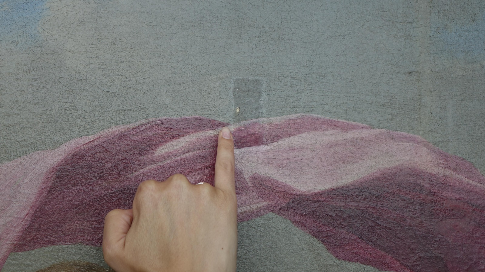 La photo montre un doigt pointant une section d'une toile où la peinture est manquante. La photo montre un doigt pointant une section d'une toile où la peinture est manquante.