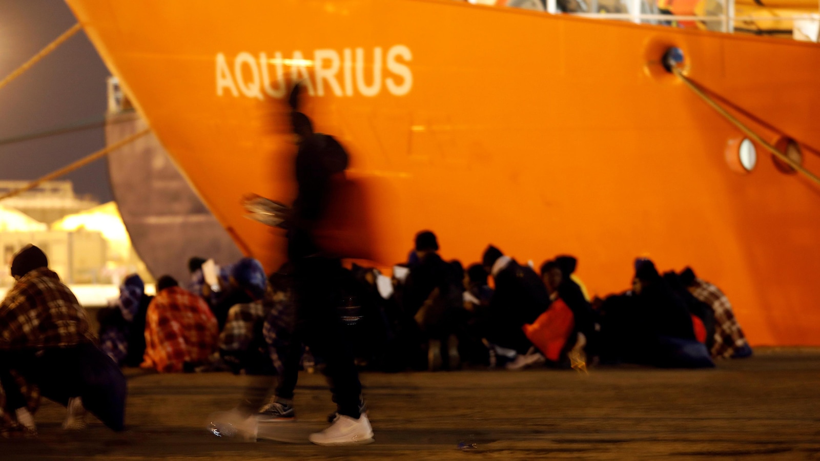 Des gens sont assis dans un port, prés du bateau de sauvetage Aquarius, amarré près d'eux. Des gens sont assis dans un port, prés du bateau de sauvetage Aquarius, amarré près d'eux.