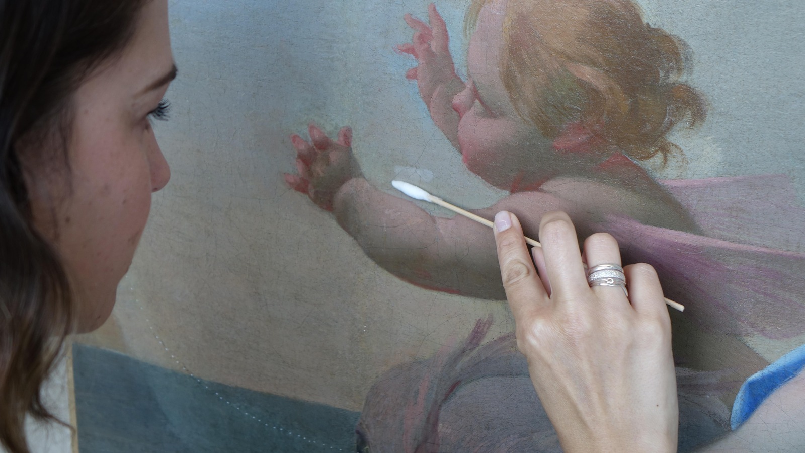 La photo montre une professionnelle qui s'affère à retirer le vernis sur une oeuvre d'art avec un coton-tige. La photo montre une professionnelle qui s'affère à retirer le vernis sur une oeuvre d'art avec un coton-tige.