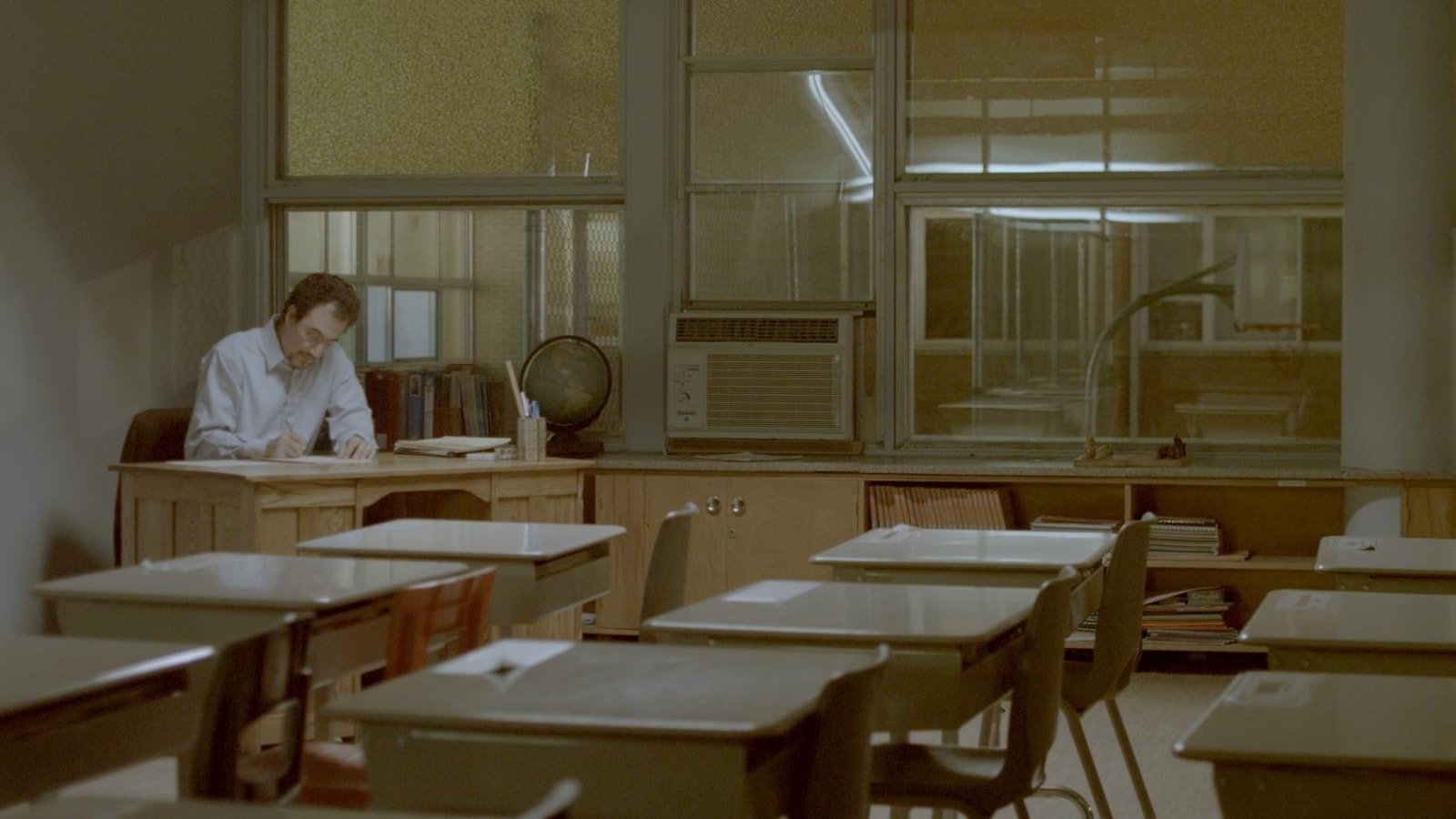 Une scène tirée du film Monsieur Lazhar où l'on voit l'acteur principal en train d'écrire seule, sur une table, assis dans une salle de classe.