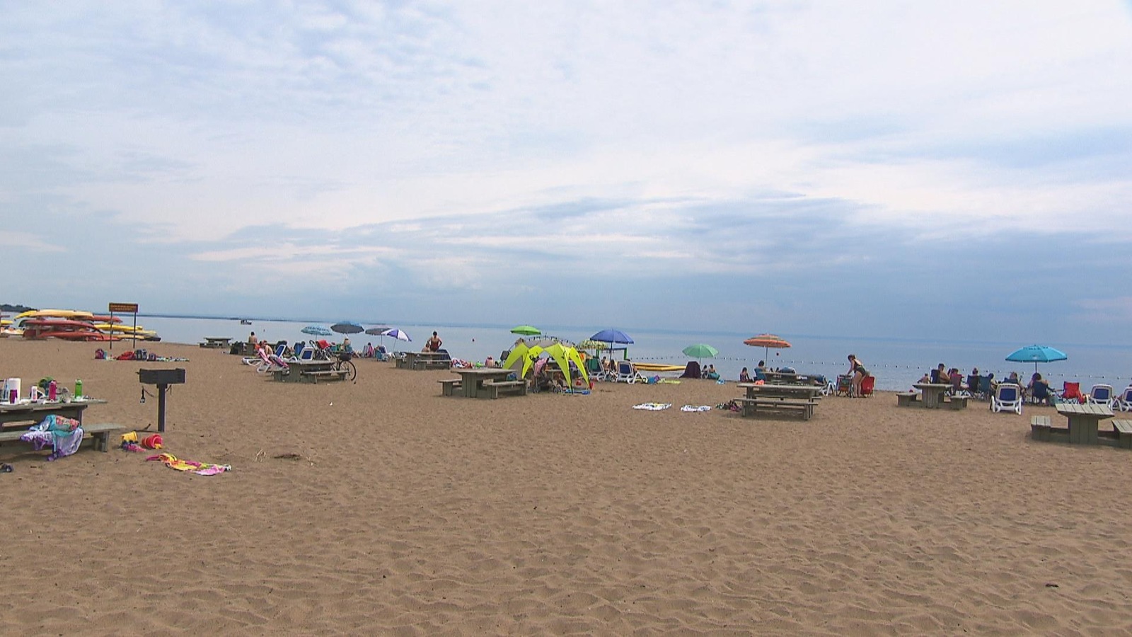 Plusieurs personnes se trouvent sur une longue plage. On peut voir le lac Saint-Jean en arrière plan. Plusieurs personnes se trouvent sur une longue plage. On peut voir le lac Saint-Jean en arrière plan.