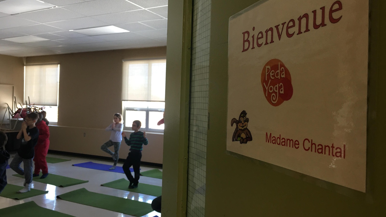 Une pancarte sur une porte souhaite la bienvenue dans la classe de pedayoga. Des élèves pratiquent le yoga en arrière-plan Une pancarte sur une porte souhaite la bienvenue dans la classe de pedayoga. Des élèves pratiquent le yoga en arrière-plan