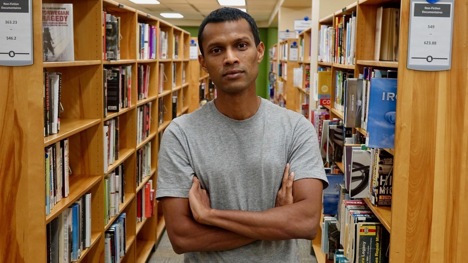 Un homme photographié dans une bibliothèque municipale, des étagères derrière lui Un homme photographié dans une bibliothèque municipale, des étagères derrière lui