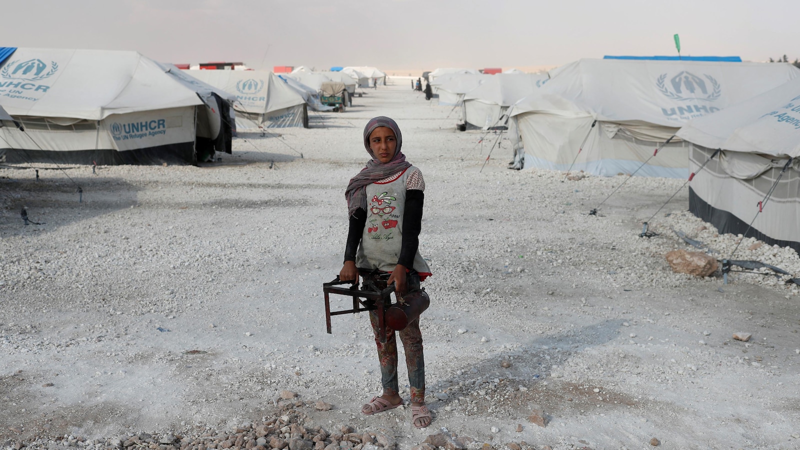 Une adolescente tient un brûleur pour faire la cuisine en plein milieu d'un camp de déplacés à Raqqa, en Syrie. Des tentes l'entourent. Une adolescente tient un brûleur pour faire la cuisine en plein milieu d'un camp de déplacés à Raqqa, en Syrie. Des tentes l'entourent.