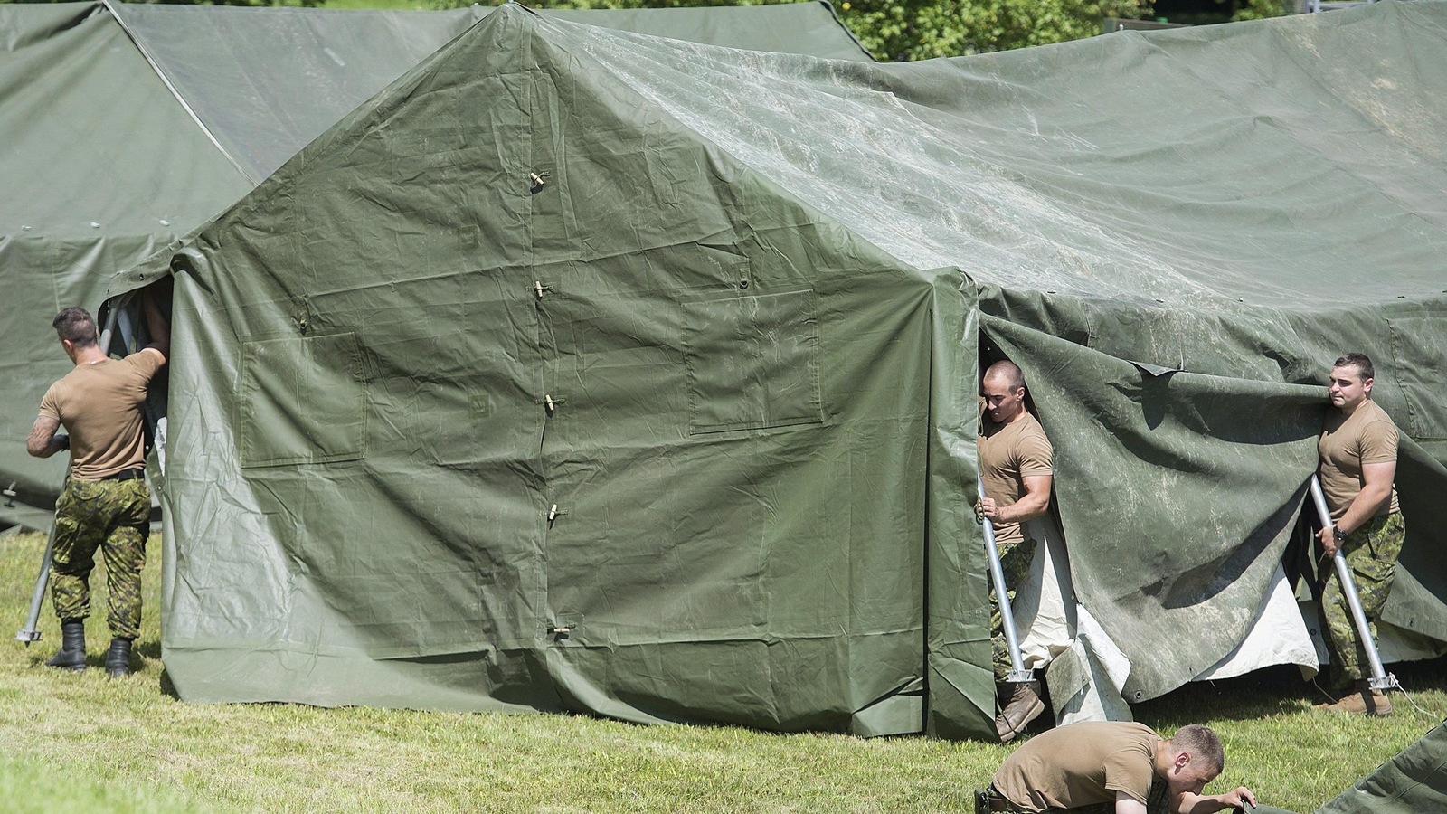 Trois militaires, dont deux tiennent des poteaux pour tendre une toile, achèvent le montage d'une tente au poste frontalier de Saint-Bernard-de-Lacolle, au Québec. Trois militaires, dont deux tiennent des poteaux pour tendre une toile, achèvent le montage d'une tente au poste frontalier de Saint-Bernard-de-Lacolle, au Québec.