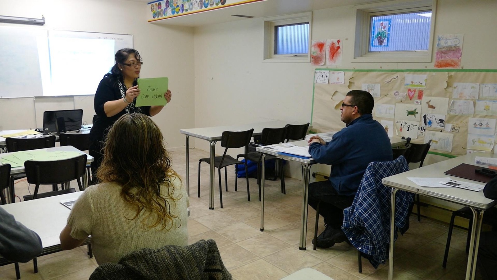 Une femme tient une carte avec un phrase en anglais devant une classe. Une femme tient une carte avec un phrase en anglais devant une classe.
