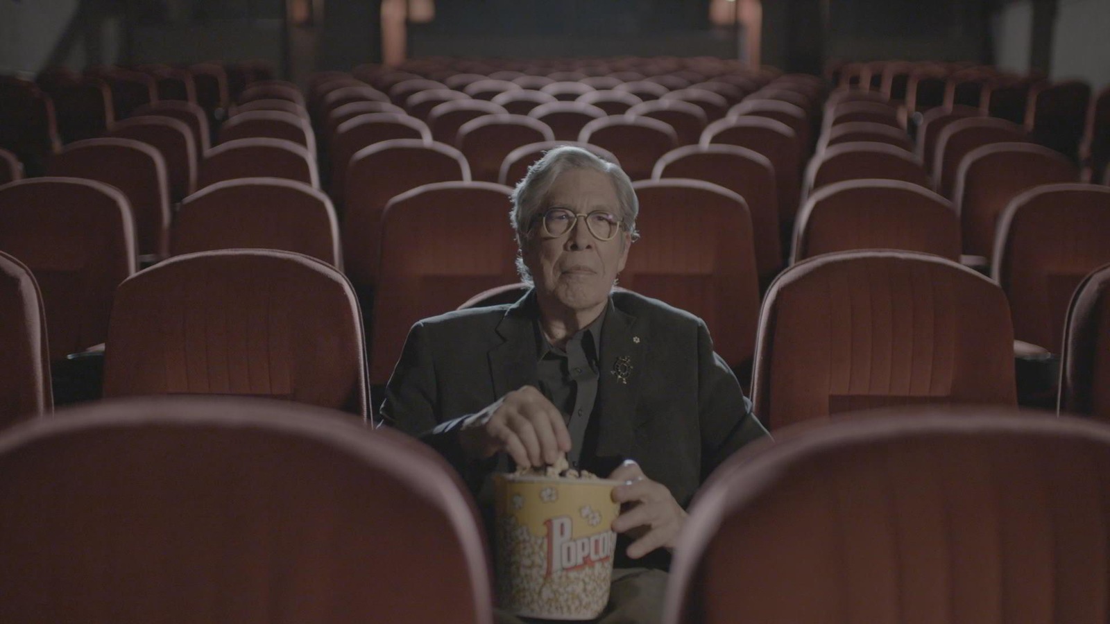 L'auteur Thomas King est dans une salle de cinéma vide et tient un pot de maïs soufflé. L'auteur Thomas King est dans une salle de cinéma vide et tient un pot de maïs soufflé.