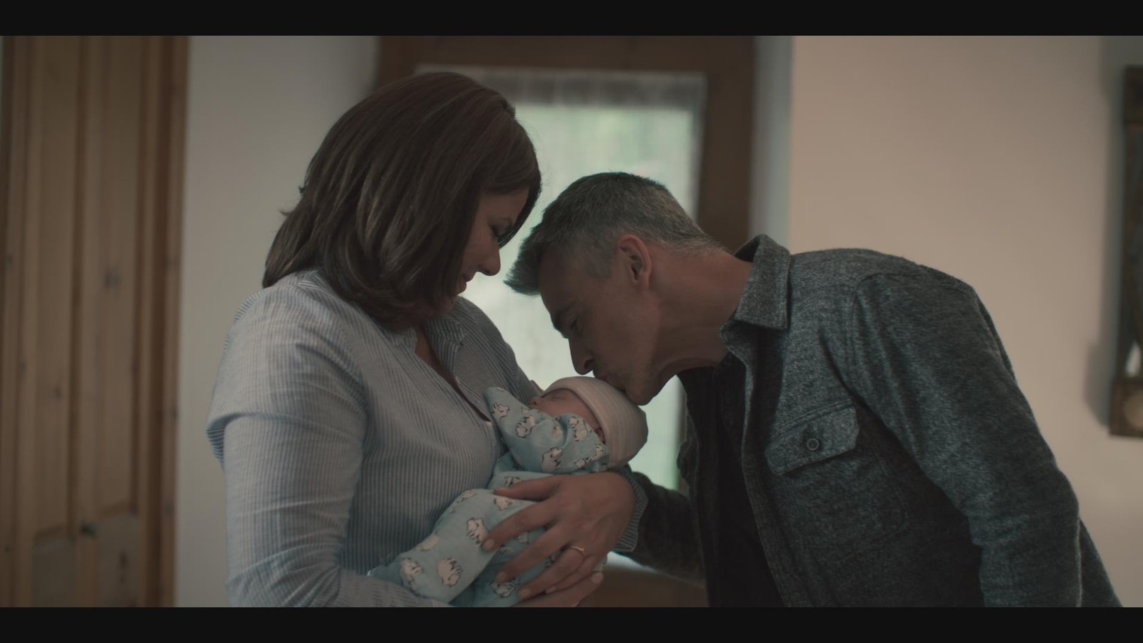 La femme tient le bébé dans ses bras, tandis que l'homme lui donne un bec sur la tête.