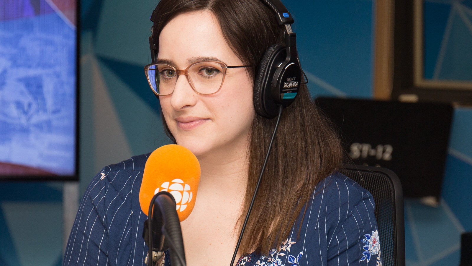 La jeune femme porte un casque d'écoute, des lunettes et regarde l'animateur. La jeune femme porte un casque d'écoute, des lunettes et regarde l'animateur.