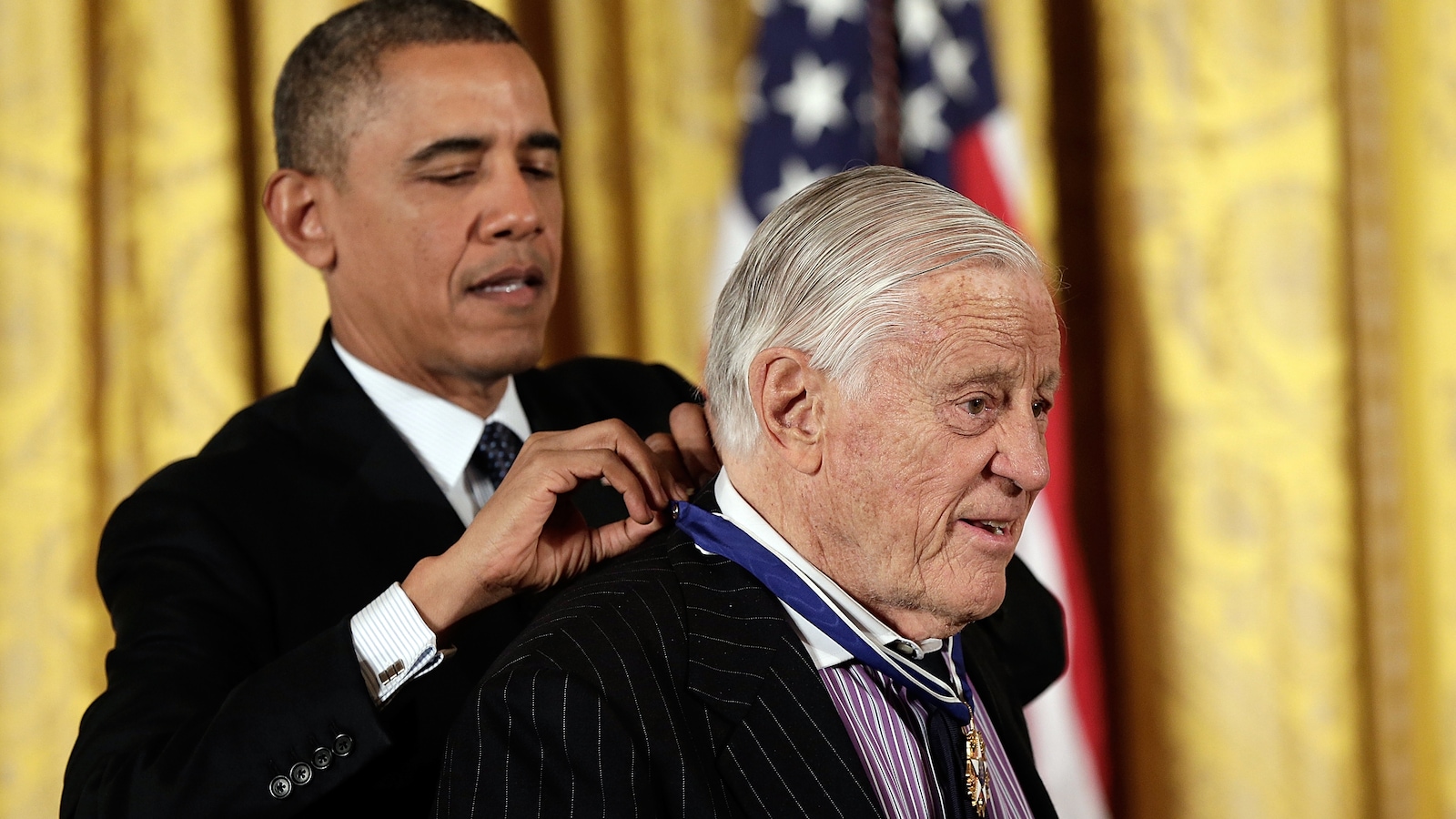 Barak Obama, debout derrière Ben Bradlee, attache une médaille à son coup. Barak Obama, debout derrière Ben Bradlee, attache une médaille à son coup.