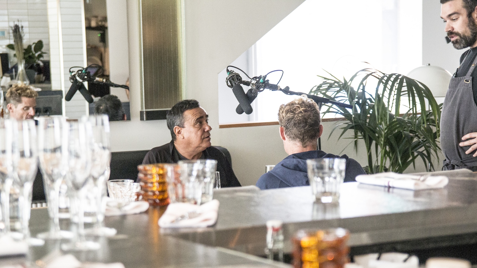 Les deux hommes sont assis à une table de restaurant et un serveur leur parle. Les deux hommes sont assis à une table de restaurant et un serveur leur parle.