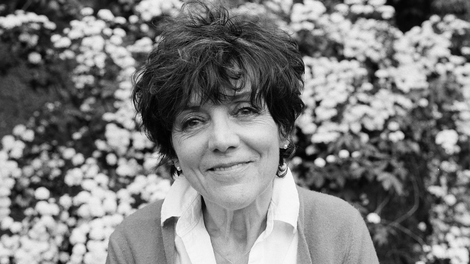 Portrait de Francine Pelletier qui sourit devant une haie fleurie. Portrait de Francine Pelletier qui sourit devant une haie fleurie.