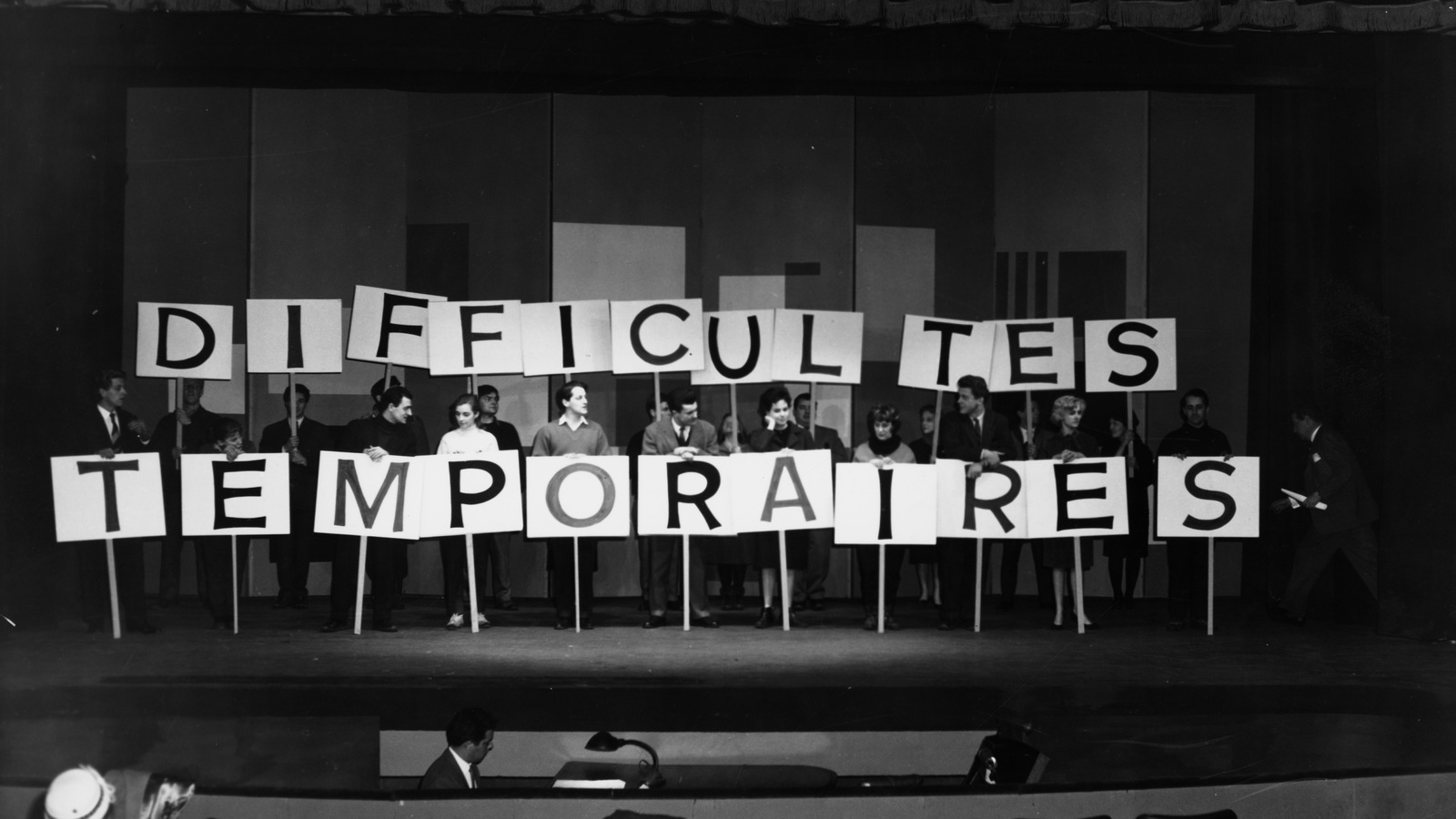 Des artistes tiennent des pancartes où il est inscrit « Difficultés temporaires ». Des artistes tiennent des pancartes où il est inscrit « Difficultés temporaires ».