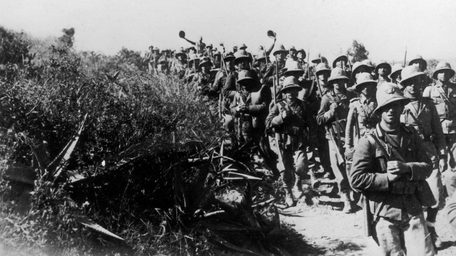 Photo en noir et blanc de soldats marchant près de buissons. Photo en noir et blanc de soldats marchant près de buissons.