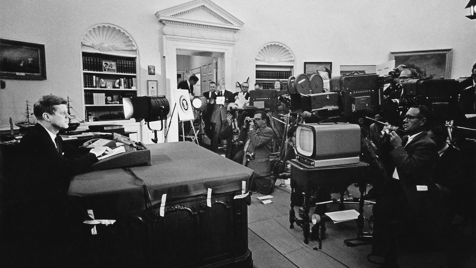 Photo en noir et blanc d'un homme assis devant un bureau. Une nuée de caméras de télévision et quelques photographes sont devant lui. Photo en noir et blanc d'un homme assis devant un bureau. Une nuée de caméras de télévision et quelques photographes sont devant lui.