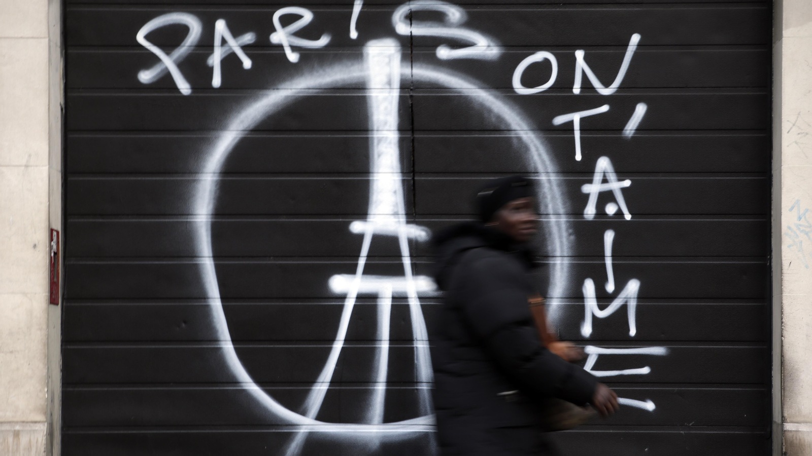 Une femme passe devant un mur où se trouve un graffiti du symbole de la paix avec la tour Eiffel devant. Une femme passe devant un mur où se trouve un graffiti du symbole de la paix avec la tour Eiffel devant.