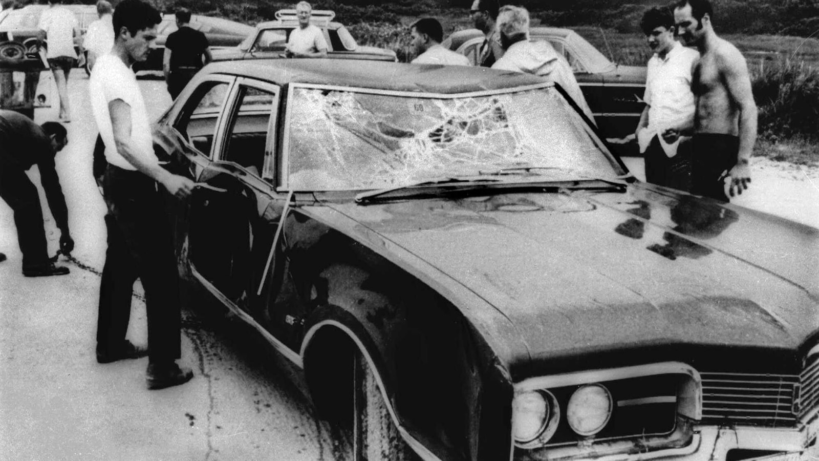 Photo en noir et blanc de trois hommes entourant une voiture accidentée. Photo en noir et blanc de trois hommes entourant une voiture accidentée.