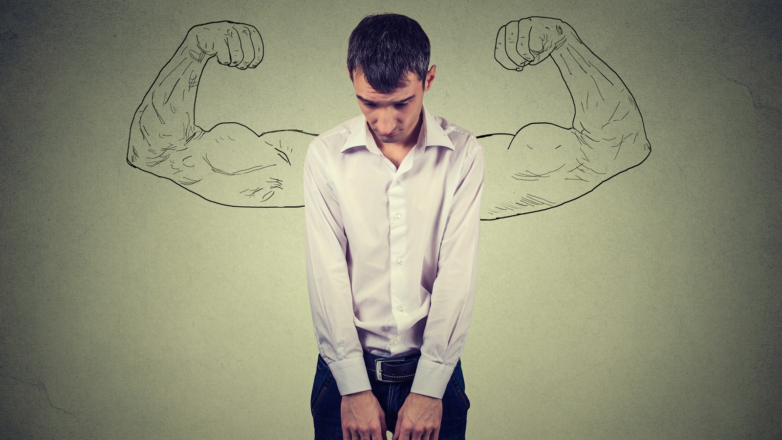 Une jeune homme mince et déprimé, la tête baissée, aimerait avoir des muscles comme ceux dessinés sur un mur derrière lui. Une jeune homme mince et déprimé, la tête baissée, aimerait avoir des muscles comme ceux dessinés sur un mur derrière lui.