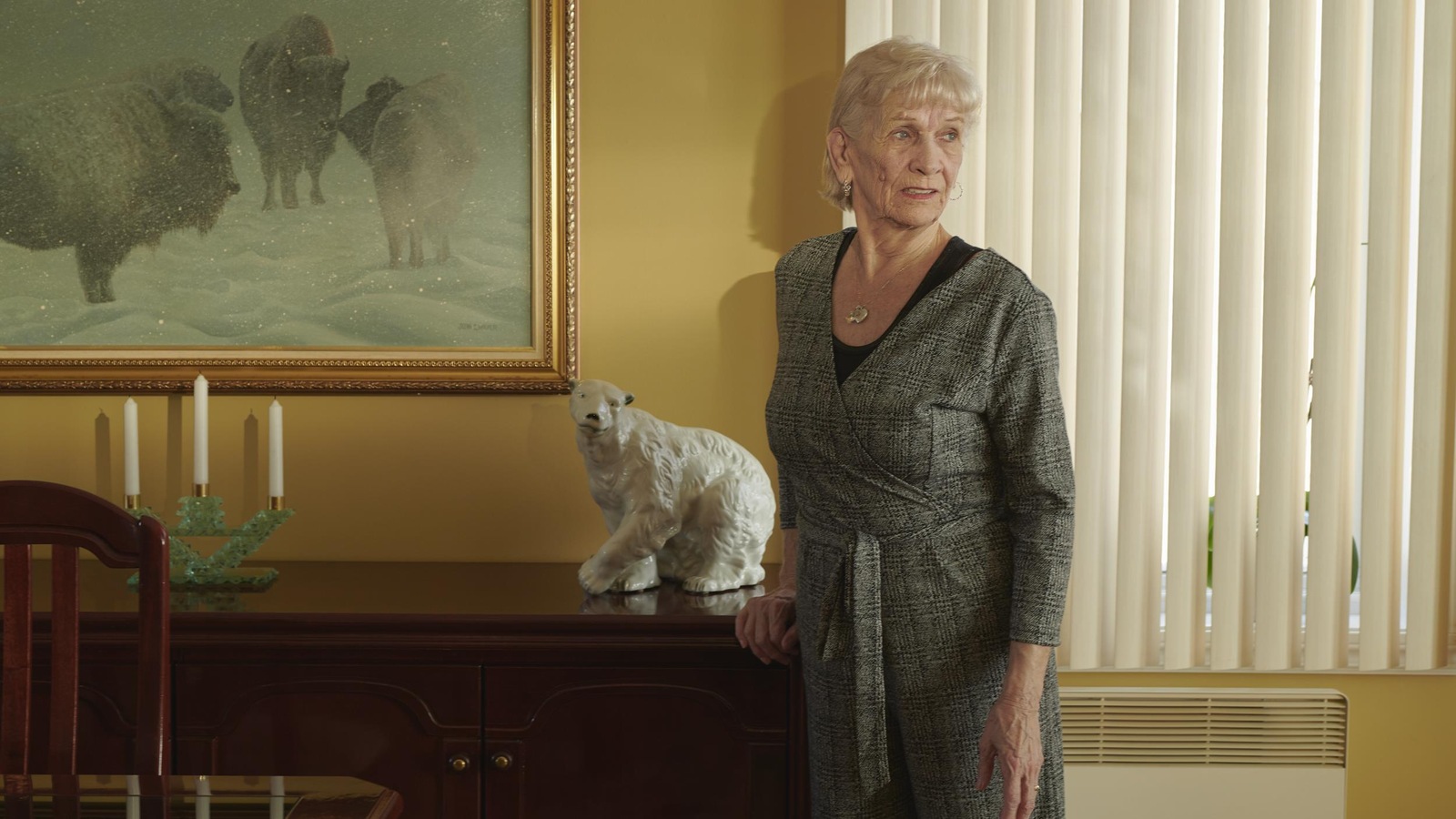 Elle est debout à côté d'un meuble sur lequel on voit une statuette d'ours polaire et des chandelles; il y a une peine sur le mur derrière elle, et il y a aussi une fenêtre derrière Norma Brown Elle est debout à côté d'un meuble sur lequel on voit une statuette d'ours polaire et des chandelles; il y a une peine sur le mur derrière elle, et il y a aussi une fenêtre derrière Norma Brown