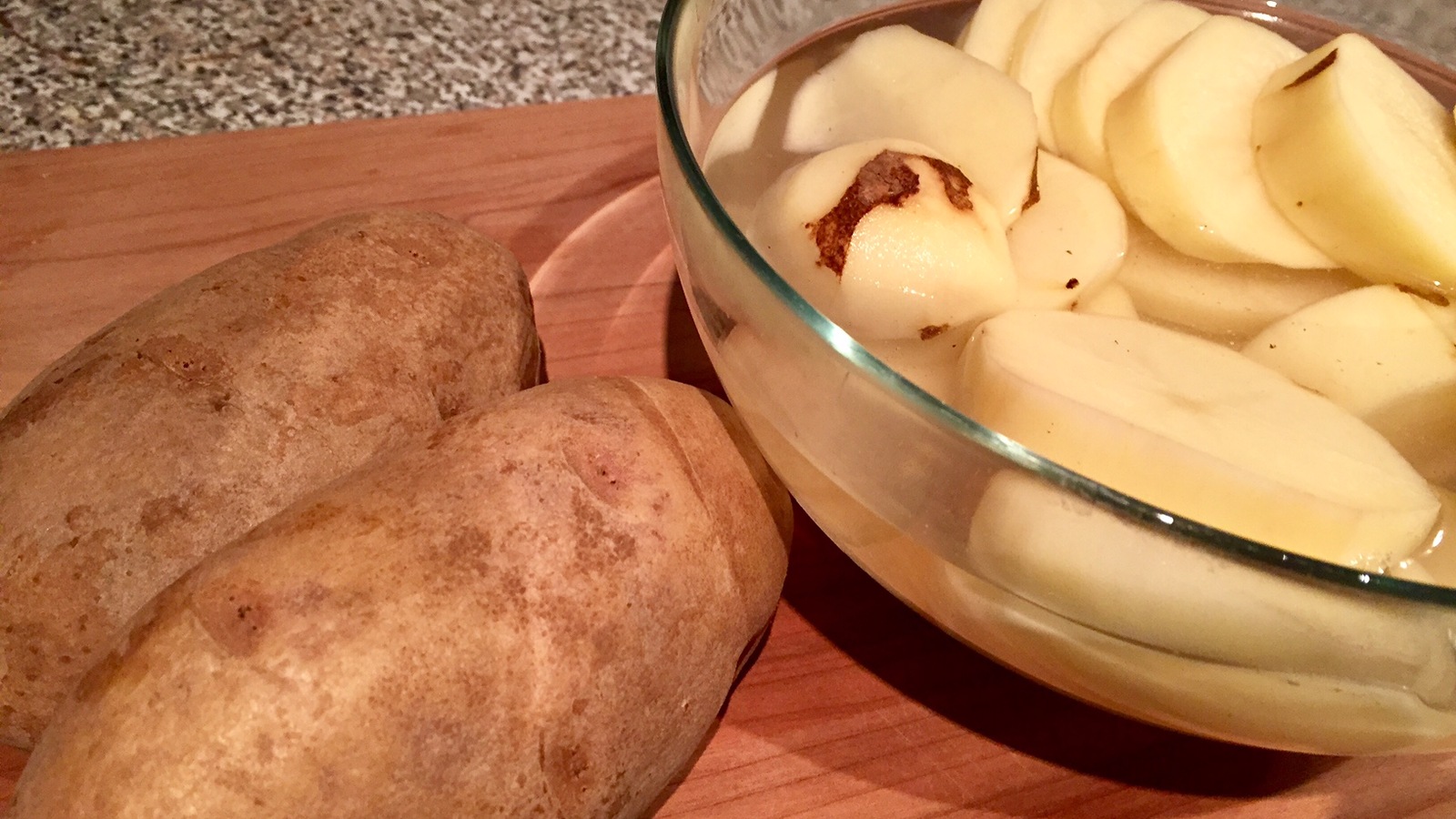Deux pommes de terre ainsi qu'un bol de pommes de terre tranchées. Deux pommes de terre ainsi qu'un bol de pommes de terre tranchées.