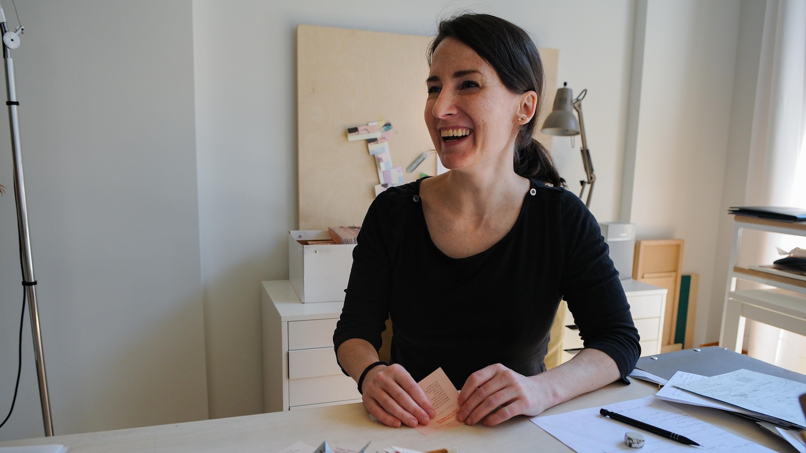 Une femme, vêtue de noir, assise à un bureau est en train de rire. Une femme, vêtue de noir, assise à un bureau est en train de rire.
