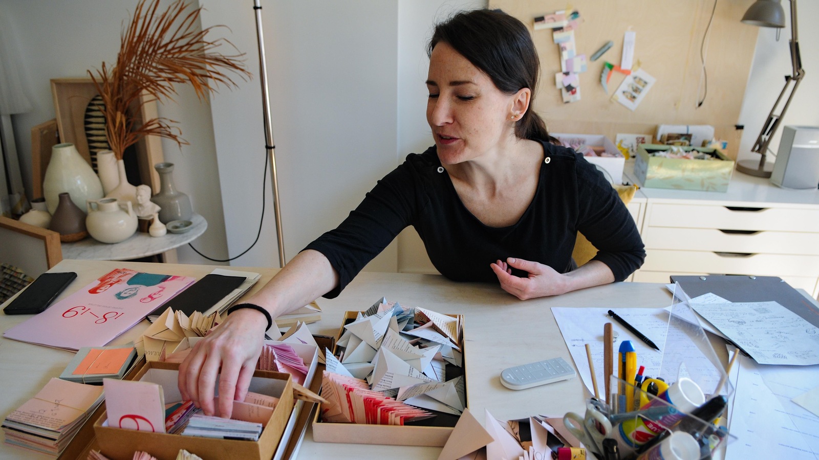 Une femme assise à son bureau pige dans une pile de papiers. Une femme assise à son bureau pige dans une pile de papiers.