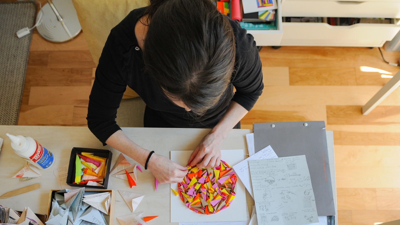Vue de haut d'une femme en train de travailler sur une œuvre de papier sur sa table de travail dans un atelier lumineux. Vue de haut d'une femme en train de travailler sur une œuvre de papier sur sa table de travail dans un atelier lumineux.