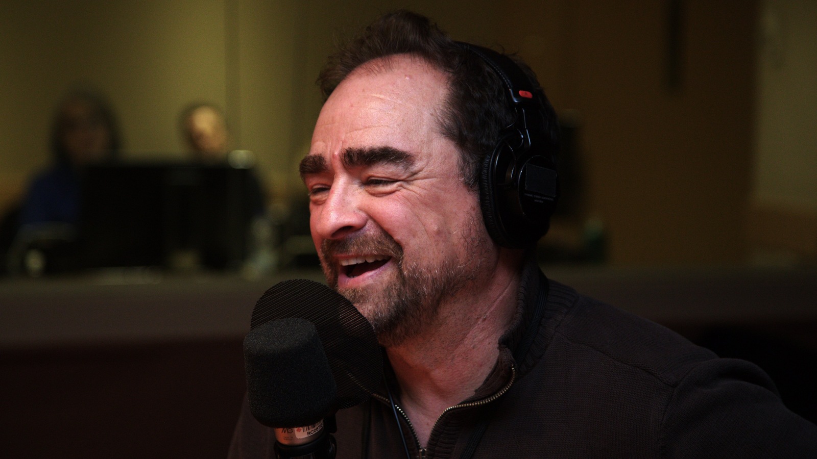 Michel Rabagliati, avec des écouteurs sur la tête, assis derrière un micro. Michel Rabagliati, avec des écouteurs sur la tête, assis derrière un micro.