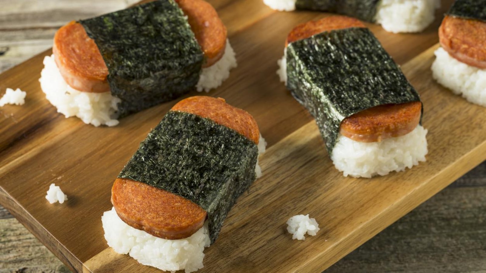 Quatre morceaux de musubi, un sushi fait avec du jambon en conserve Spam, sur une planche de bois. Quatre morceaux de musubi, un sushi fait avec du jambon en conserve Spam, sur une planche de bois.