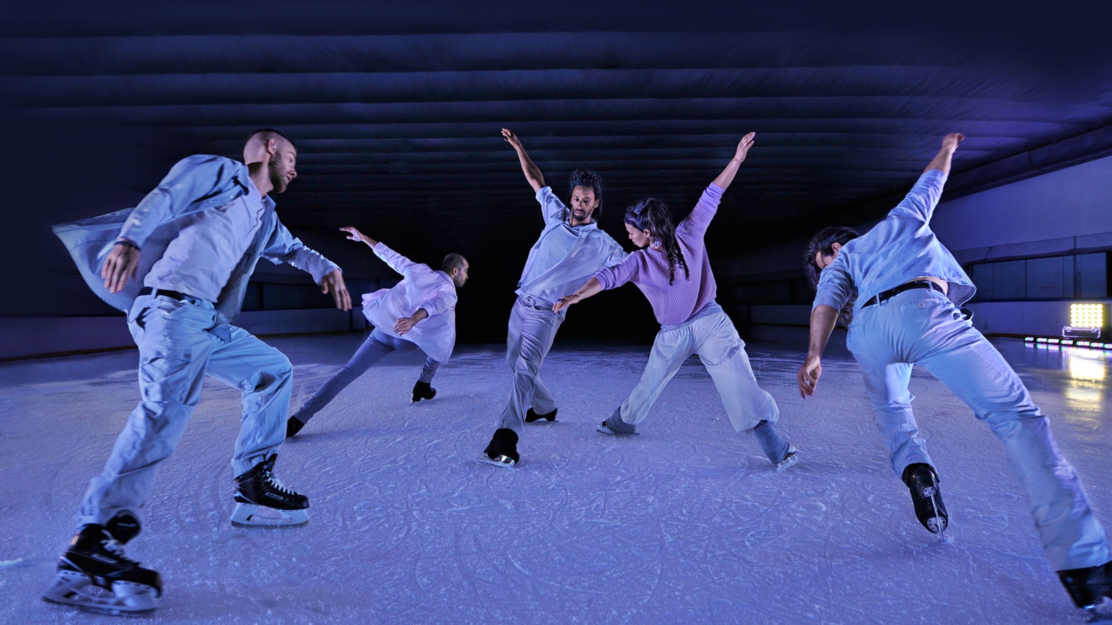 Des danseurs-patineurs font une figure, jambes amplement écartées, bras en croix, sous un éclairage bleuté Des danseurs-patineurs font une figure, jambes amplement écartées, bras en croix, sous un éclairage bleuté