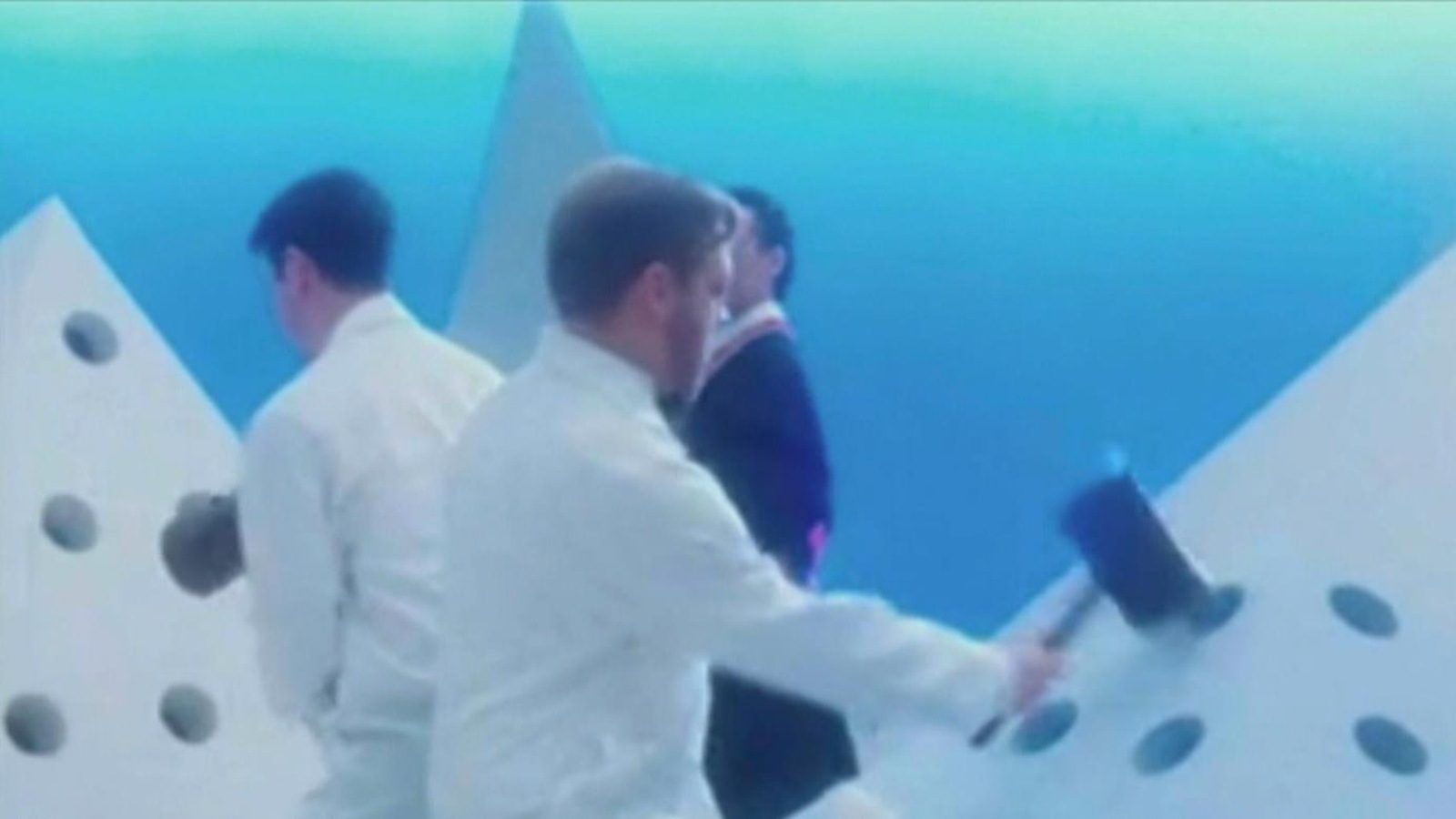 Des hommes en blanc frappent sur des prismes troués desquels sortent des têtes de phoques ensanglantées. Des hommes en blanc frappent sur des prismes troués desquels sortent des têtes de phoques ensanglantées.