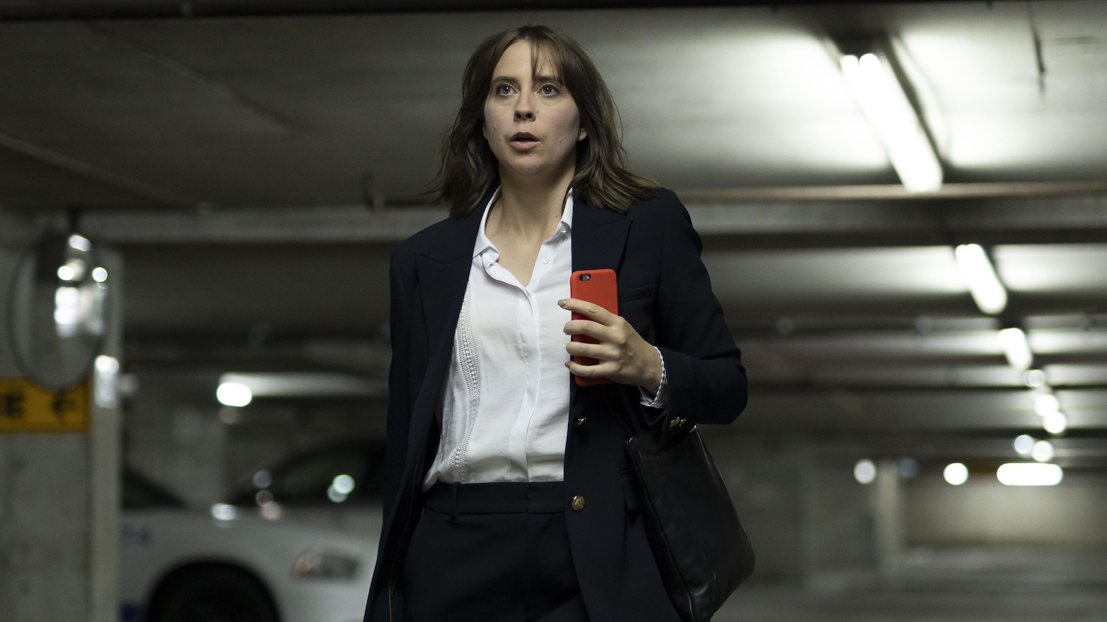 Gabrielle Laflamme (Eve Landry) marche dans un stationnement souterrain en traînant sa valise à roulettes.