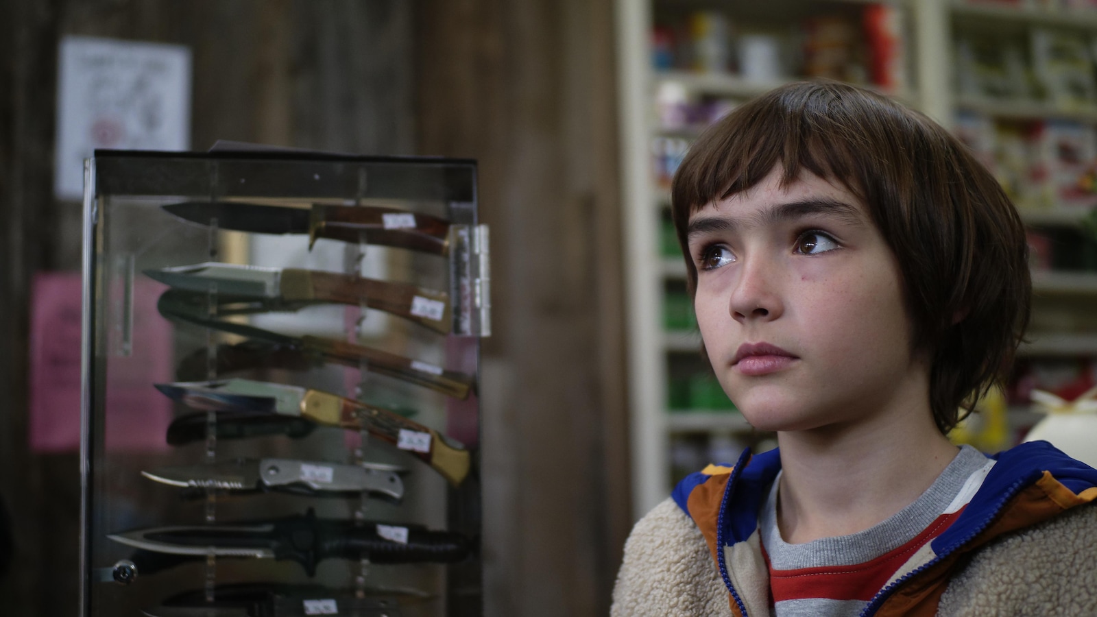 Un jeune garçon dans un magasin, à côté d'un présentoir de couteaux. Un jeune garçon dans un magasin, à côté d'un présentoir de couteaux.