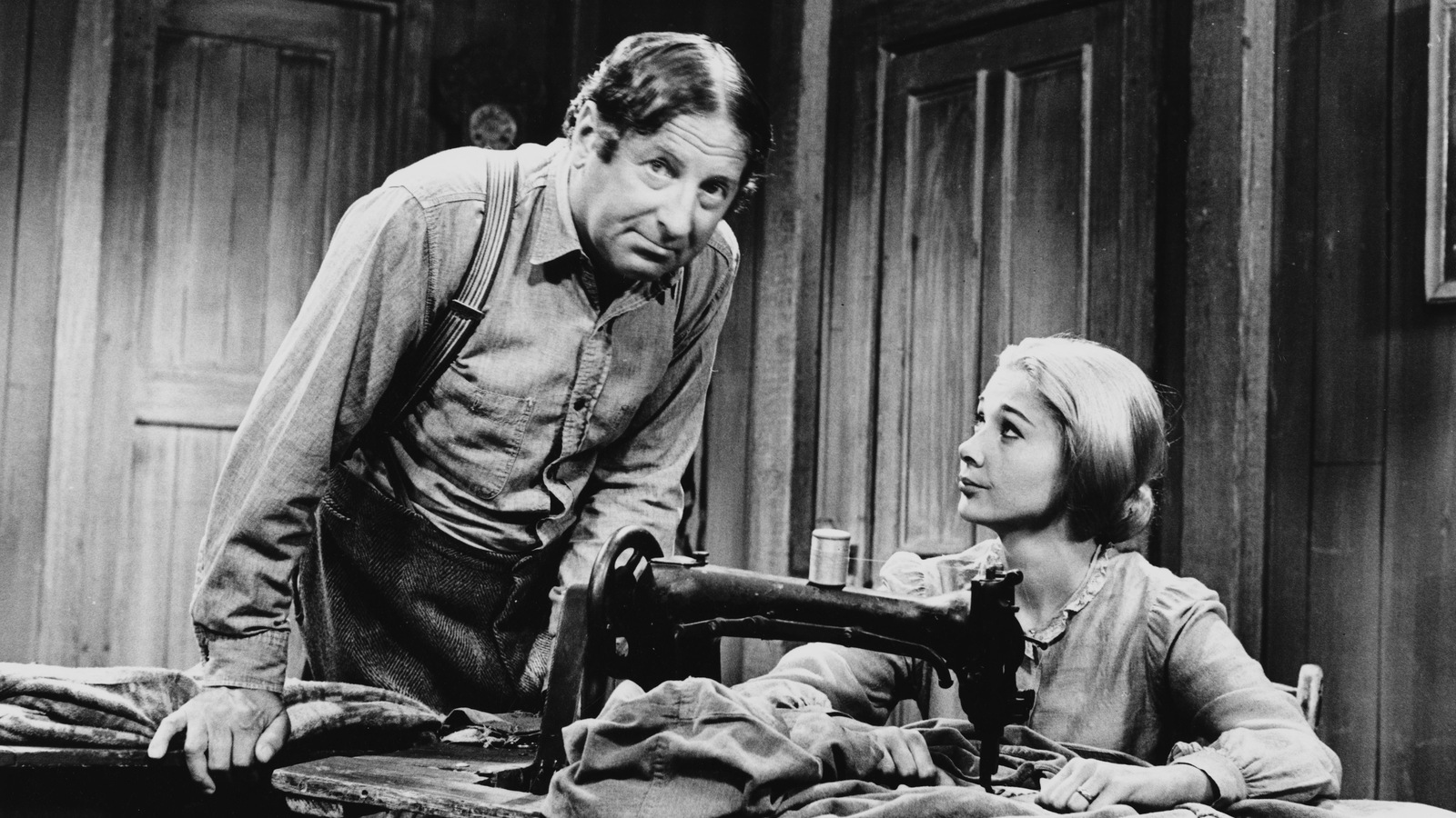 Dans leur maison, Séraphin (Jean-Pierre Masson) se penche vers Donalda (Andrée Champagne) qui est assise derrière un moulin à coudre. Dans leur maison, Séraphin (Jean-Pierre Masson) se penche vers Donalda (Andrée Champagne) qui est assise derrière un moulin à coudre.