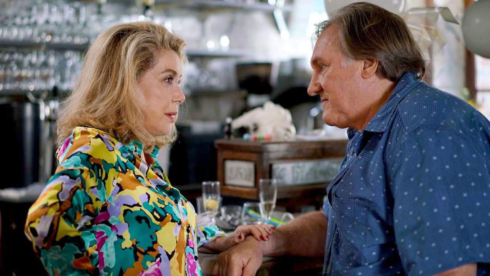 Une femme (Catherine Deneuve) avec un chemisier coloré et un homme (Gérard Depardieu) en chemise bleue se font face, devant le comptoir d'un bar. Une femme (Catherine Deneuve) avec un chemisier coloré et un homme (Gérard Depardieu) en chemise bleue se font face, devant le comptoir d'un bar.