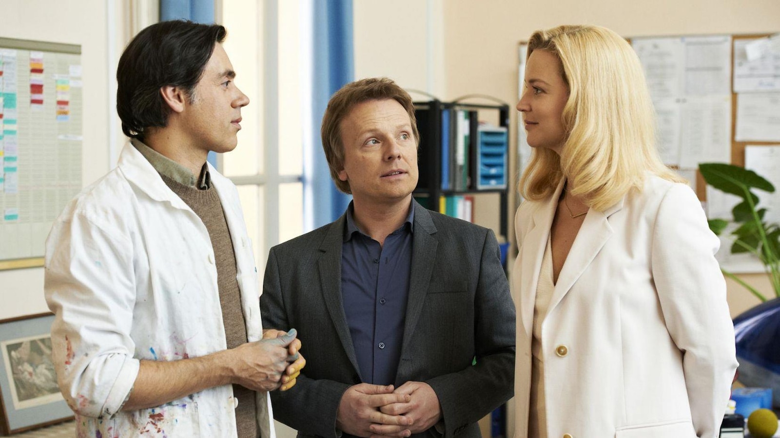 Un homme en blouse blanche (Emmanuel Mouret) aux côtés d'un autre homme regarde une femme blonde (Virginie Effira). Un homme en blouse blanche (Emmanuel Mouret) aux côtés d'un autre homme regarde une femme blonde (Virginie Effira).