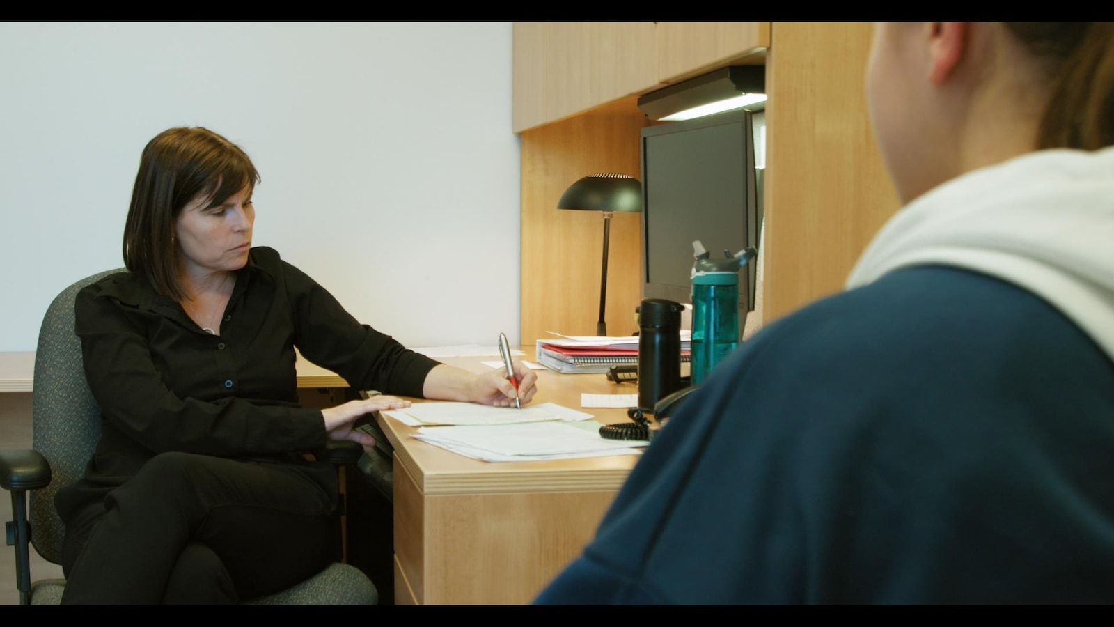 La femme est assise et écrit sur une feuille à son bureau.