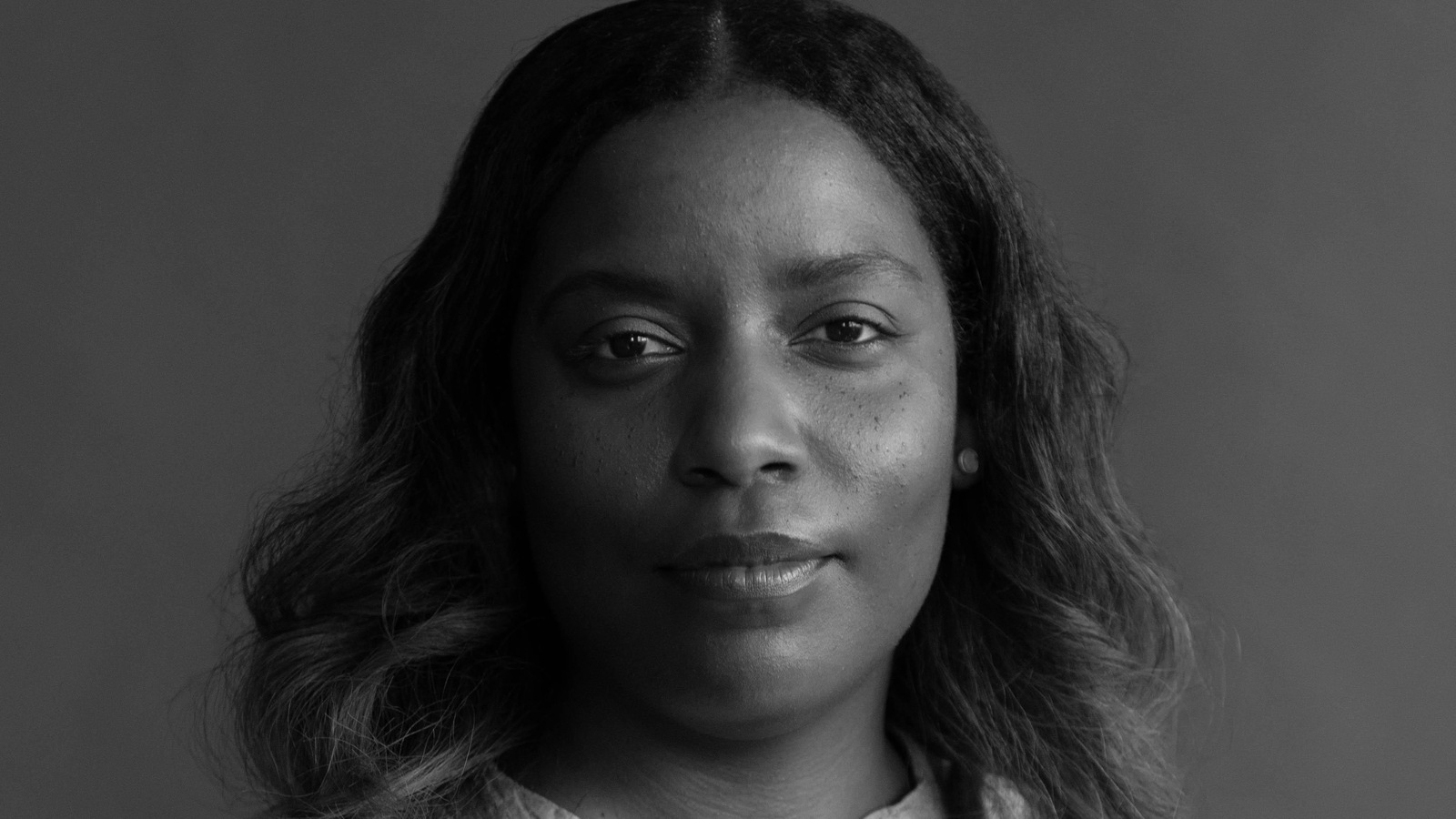 Sur fond gris et en noir et blanc, une femme regarde droit devant elle.