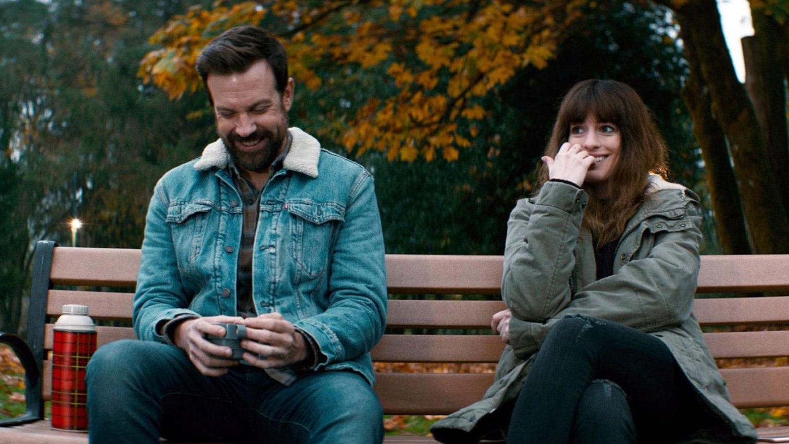 Un homme et une femme (Anne Hathaway) assis sur un banc, rient.