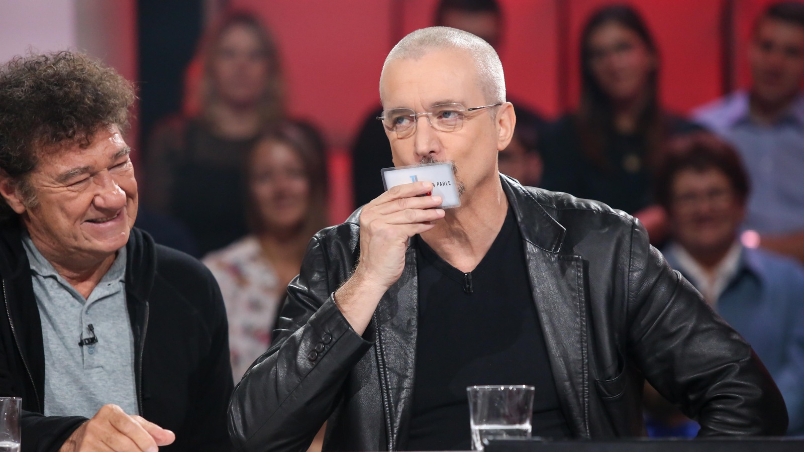 Dan Bigras porte une veste de cuir noire. Robert Charlebois est assis à sa gauche. Dan Bigras porte une veste de cuir noire. Robert Charlebois est assis à sa gauche.
