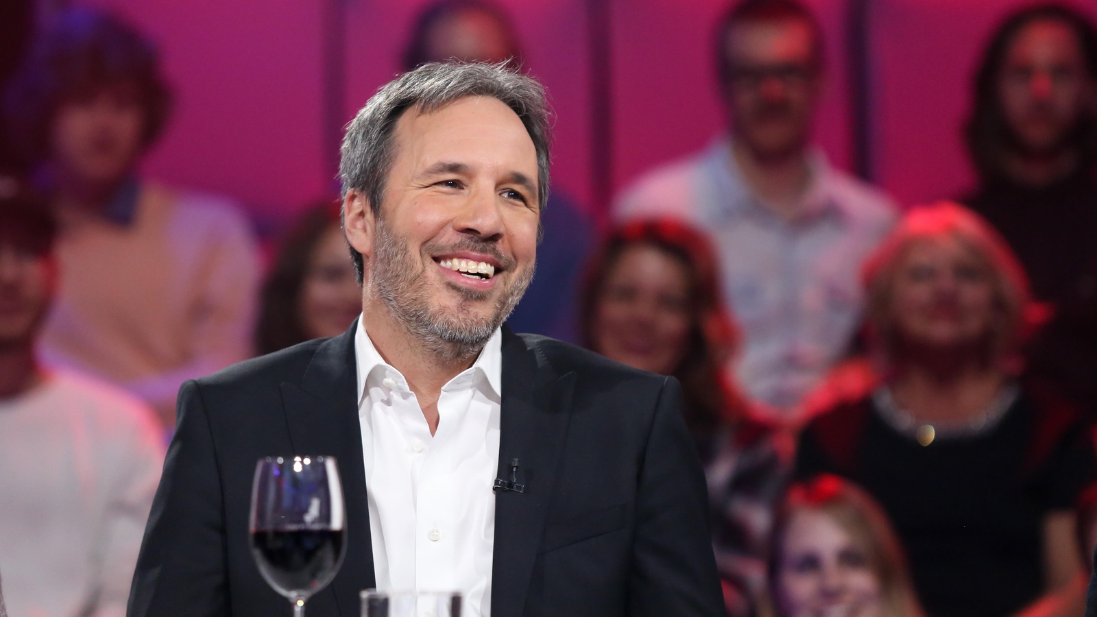 Il sourit. Il porte une chemise blanche et un veston noir. Il sourit. Il porte une chemise blanche et un veston noir.