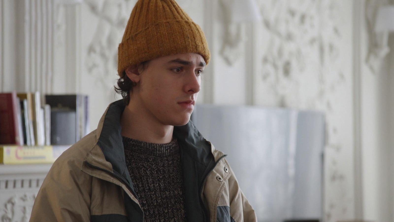 Un jeune homme qui porte un manteau beige et bleu marin et une tuque or. Un jeune homme qui porte un manteau beige et bleu marin et une tuque or.