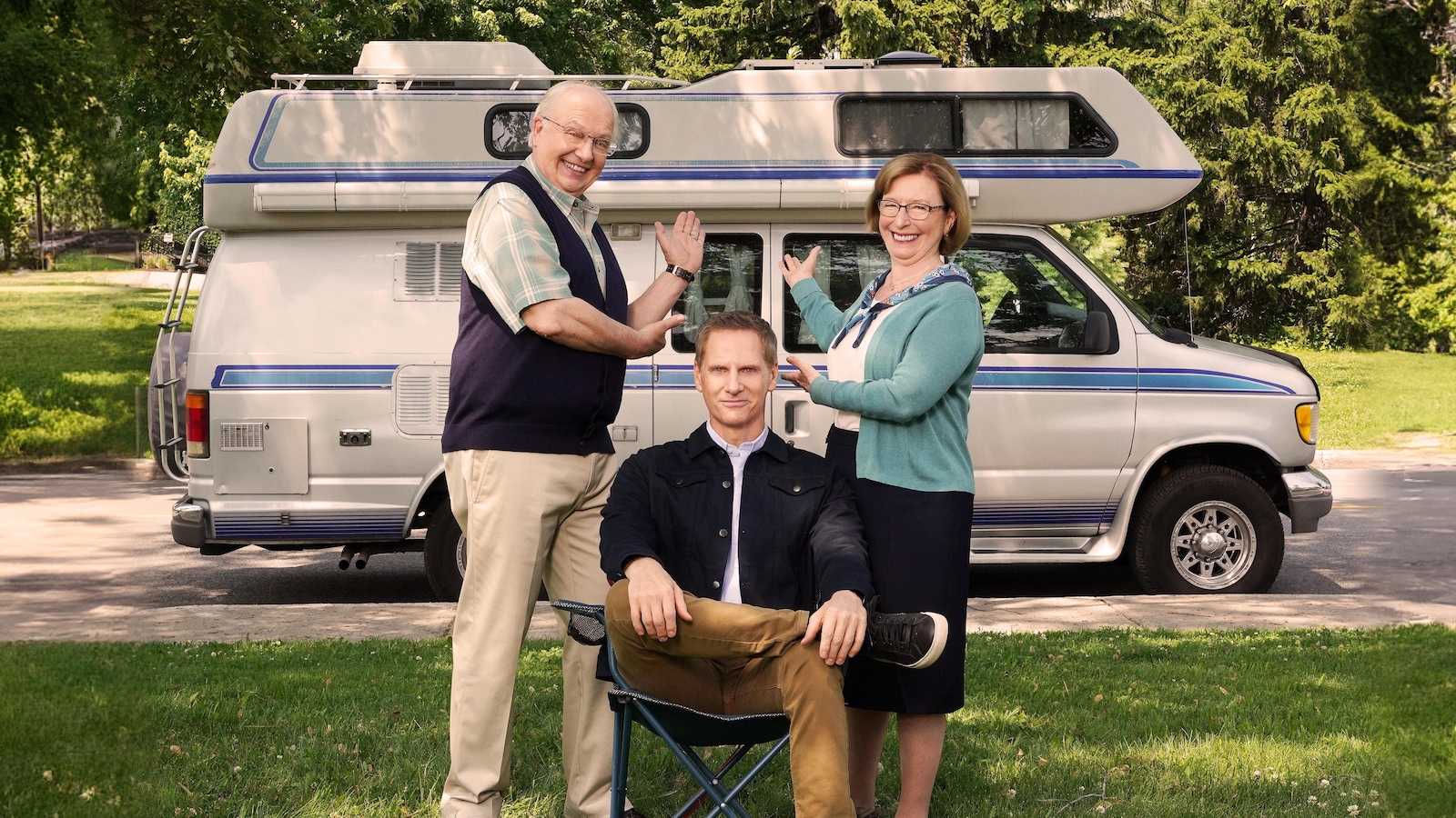 François est assis dans une chaise de camping; ses parents debout de chaque côté montre leur véhicule récréatif.