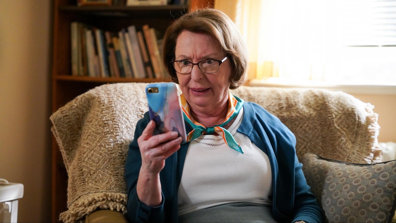 Rollande (Marie-Ginette Guay) regarde son téléphone intelligent avec un air incrédule.