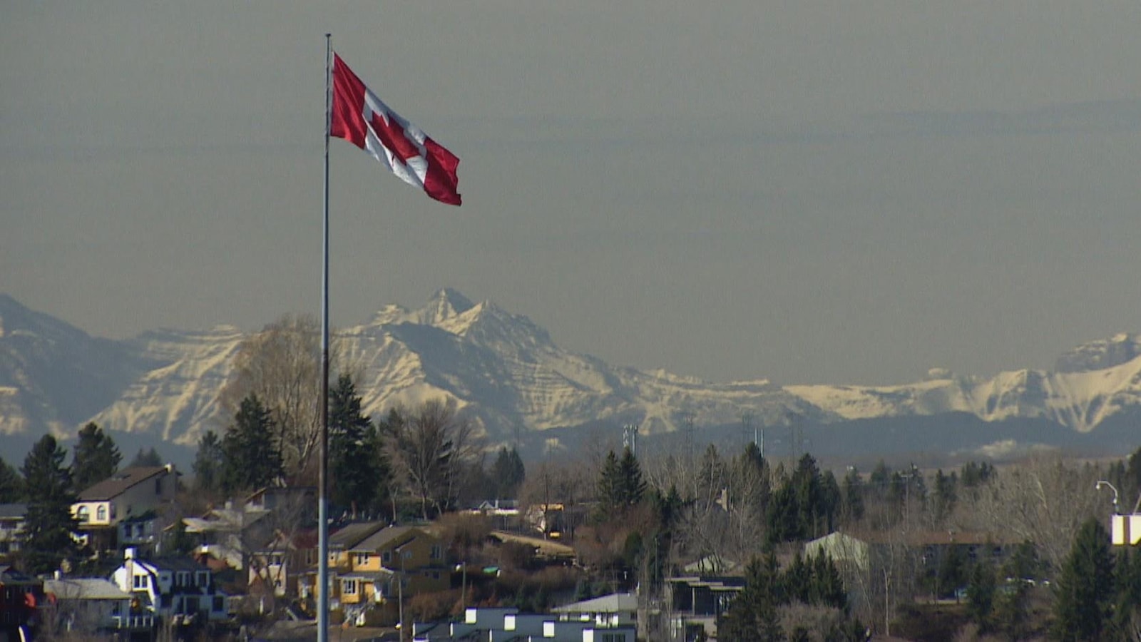 Un drapeau canadien flotte au vent, les Rocheuses canadiennes sont en arrière-plan.