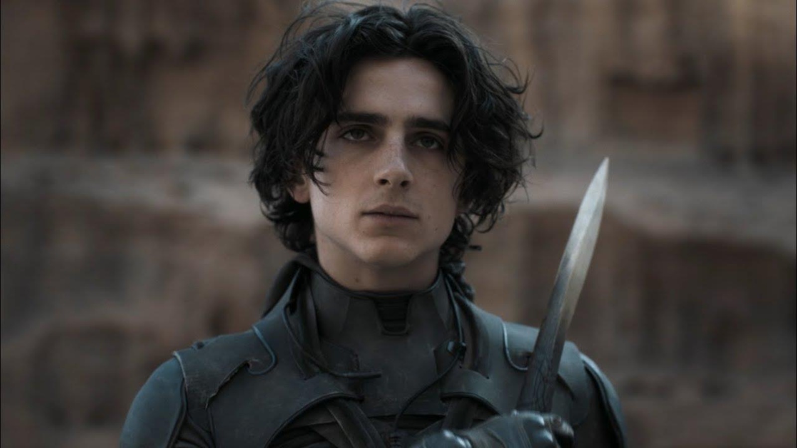 Un jeune homme (Timothée Chalamet) portant une tenue de combat et un poignard. Un jeune homme (Timothée Chalamet) portant une tenue de combat et un poignard.