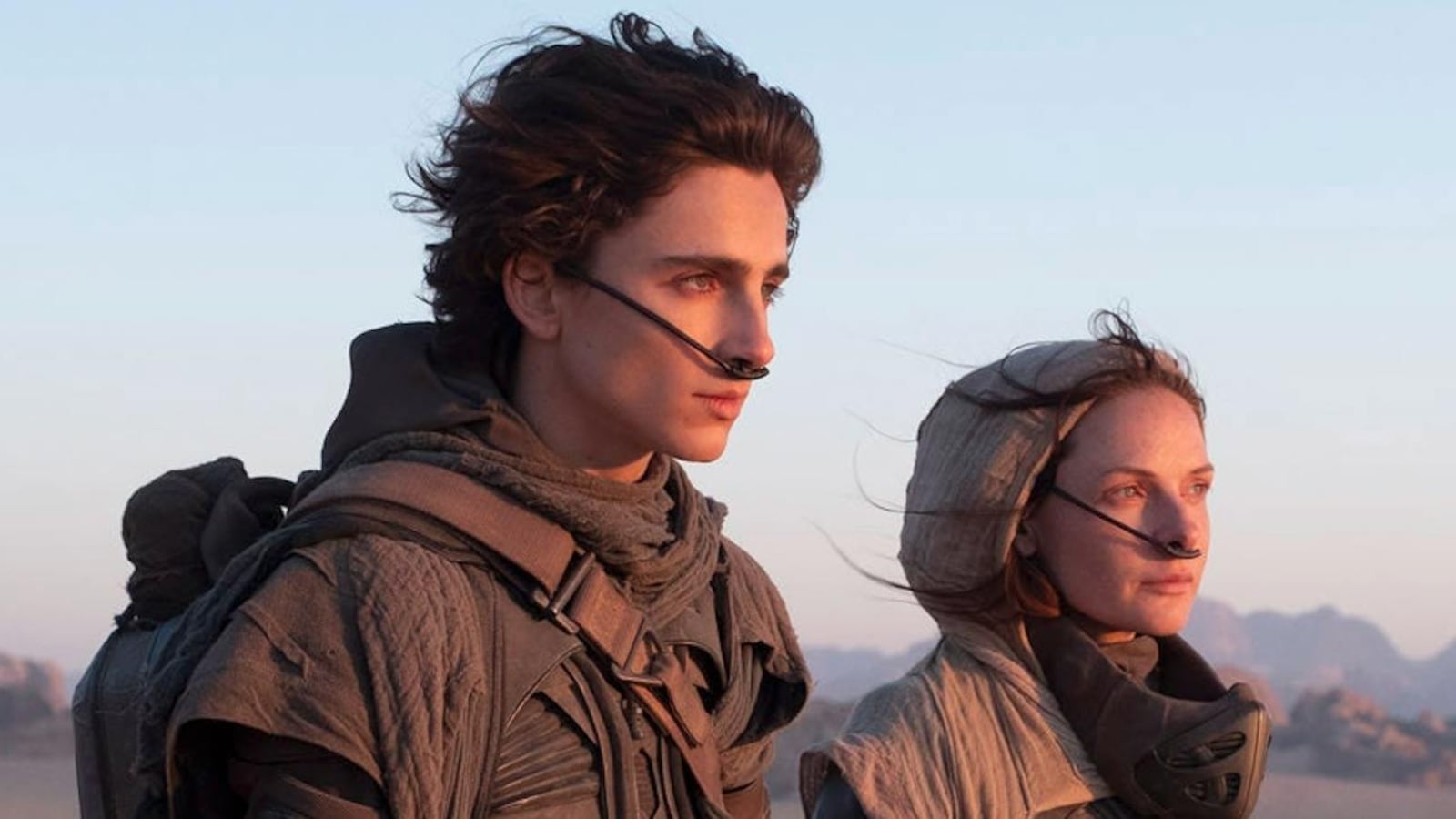 Un jeune homme (Timothée Chalamet) et une femme (Rebecca Ferguson) avec des systèmes de respiration dans le nez regardent vers l'horizon à droite. Un jeune homme (Timothée Chalamet) et une femme (Rebecca Ferguson) avec des systèmes de respiration dans le nez regardent vers l'horizon à droite.